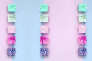 Small gift boxes of different colors with ribbons lies on a violet and pink background photo