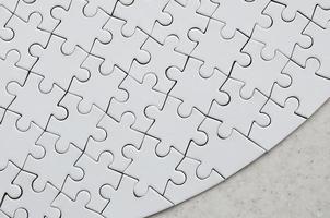A white jigsaw puzzle in the complete form lies on a treated stone surface. Textured image with copy space photo