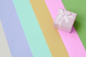 Small pink gift box lie on texture background of fashion pastel pink, blue, green, yellow, violet and beige colors photo