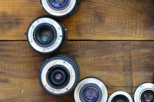 Several photographic lenses lie on a brown wooden background. Space for text photo