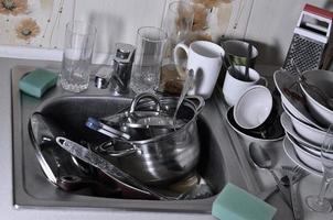 A huge pile of unwashed dishes in the kitchen sink and on the countertop photo