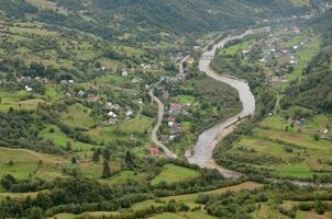 A beautiful view of the village of Mezhgorye, Carpathian region. A lot of residential buildings surrounded by high forest mountains and long river photo