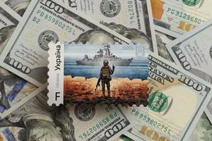 TERNOPIL, UKRAINE - SEPTEMBER 2, 2022 Famous Ukrainian postmark with russian warship and ukrainian soldier as wooden souvenir on big amount of US dollar bills photo