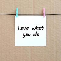 Love what you do. Note is written on a white sticker that hangs with a clothespin on a rope on a background of brown cardboard photo