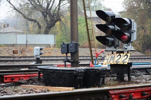 Photo of a fragment of a railway track with a small traffic light in rainy weather