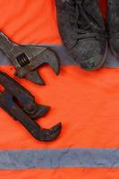 Adjustable wrenches and old boots lies on an orange signal worker shirt photo