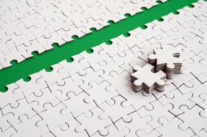 The green path is laid on the platform of a white folded jigsaw puzzle. The missing elements of the puzzle are stacked nearby. Texture image with space for text photo