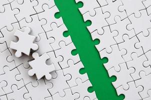 The green path is laid on the platform of a white folded jigsaw puzzle. The missing elements of the puzzle are stacked nearby. Texture image with space for text photo
