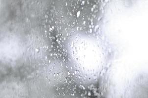 A photo of rain drops on the window glass with a blurred view of the blossoming green trees. Abstract image showing cloudy and rainy weather conditions