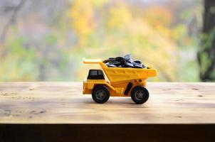 A small yellow toy truck is loaded with sunflower seeds. A car on a wooden surface against a background of autumn forest. Extraction and transportation of sunflower seeds photo