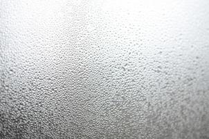 A photo of the glass surface of the window, covered with a multitude of droplets of various sizes. Background texture of a dense layer of condensate on glass