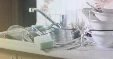 A huge pile of unwashed dishes in the kitchen sink and on the countertop photo