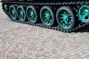 A military vehicle on caterpillar tracks stands on a square of paving stones. Photo of green caterpillars with metal wheels that rotate them