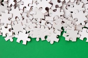 A pile of uncombed elements of a white jigsaw puzzle lies on the background of a green surface. Texture photo with copy space for text