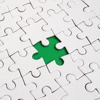 Close-up texture of a white jigsaw puzzle in assembled state with missing elements forming a green pad for text. Copy space photo