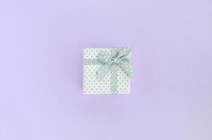 Small white gift box with ribbon lies on a violet background. Minimalism flat lay top view photo