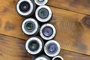 Several photographic lenses lie on a brown wooden background. Space for text photo