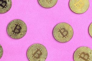 Many golden bitcoins lies on a blanket made of soft and fluffy light pink fleece fabric. Physical visualization of virtual crypto currency photo