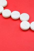 A few white tablets lie on a bright red background surface. Background image on medical and pharmaceutical topics photo