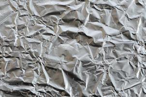 Thin wrinkled sheet of crushed tin aluminum silver foil background with shiny crumpled surface for texture photo