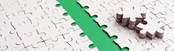 The green path is laid on the platform of a white folded jigsaw puzzle. The missing elements of the puzzle are stacked nearby. Texture image with space for text photo