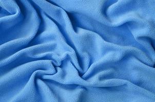 The blanket of furry blue fleece fabric. A background of light blue soft plush fleece material with a lot of relief folds photo