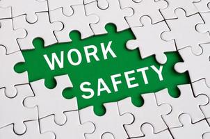 White jigsaw puzzle in assembled state with missing elements forming a green space with white inscription. Work safety photo