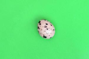 One quail egg on a light green surface, top view, empty place fo photo