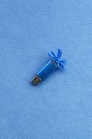 la tarjeta de memoria flash usb azul brillante con un lazo azul se encuentra sobre una manta de tela de vellón azul claro suave y peluda. diseño clásico de regalo femenino para una tarjeta de memoria foto