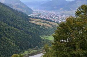 A beautiful view of the village of Mezhgorye, Carpathian region. A lot of residential buildings surrounded by high forest mountains and long river photo