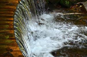 Handmade wooden water drains from small treated beams. A beautiful fragment of a small waterfall photo