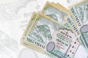 Los billetes de 100 rupias nepalíes se encuentran apilados sobre el fondo de un gran billete semitransparente. presentación abstracta de la moneda nacional foto