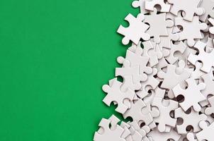 A pile of uncombed elements of a white jigsaw puzzle lies on the background of a green surface. Texture photo with copy space for text