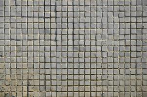 la textura del antiguo muro de hormigón, con un revestimiento de baldosas poco profundas de forma cuadrada, pintadas de gris. imagen de fondo de una pared de muchas baldosas blancas cuadradas foto