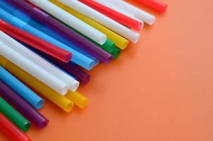 Many colorful straws for drinks lies on a bright orange background surface photo