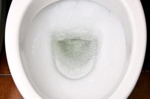 A photo of a white ceramic toilet bowl in the process of washing it off. Ceramic sanitary ware for correcting the need with an automatic flushing device