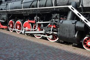 ruedas de la vieja locomotora de vapor negra de la época soviética. el lado de la locomotora con elementos de la tecnología giratoria de trenes antiguos foto