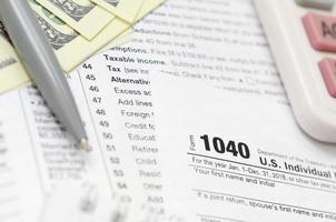 el bolígrafo, el cuaderno, la calculadora y los billetes de dólar se encuentran en el formulario de impuestos 1040 de la declaración de impuestos sobre la renta de las personas físicas. la hora de pagar impuestos foto