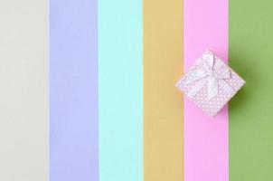 Small pink gift box lie on texture background of fashion pastel pink, blue, green, yellow, violet and beige colors photo