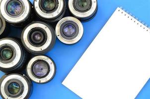 Several photographic lenses and white notebook lie on a bright blue background. Space for text photo