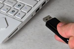 A male hand inserts a black compact USB card into the corresponding input in the side of the white netbook. Man uses modern technologies to store memory and digital data photo