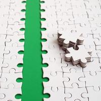 The green path is laid on the platform of a white folded jigsaw puzzle. The missing elements of the puzzle are stacked nearby. Texture image with space for text photo
