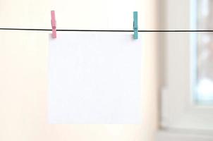 White blank cards on rope, light wall background. Creative reminder, small sheets of paper on old clothespin, memo backdrop photo