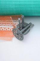 A set of construction items for the insulation of walls. Plastic dowels, a roll of mesh for the insulation of facades and a corner profile with a grid lie on the foam polystyrene surface photo