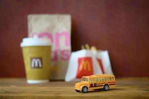 KHARKOV, UKRAINE - DECEMBER 9, 2020 Small school bus and McDonald's junk food on wooden table photo