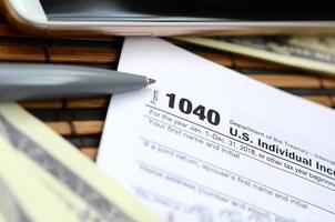 The pen, notebook, smartphone and dollar bills is lies on the tax form 1040 U.S. Individual Income Tax Return. The time to pay taxes photo