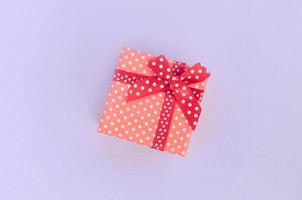 Small red gift box with ribbon lies on a violet background. Minimalism flat lay top view photo