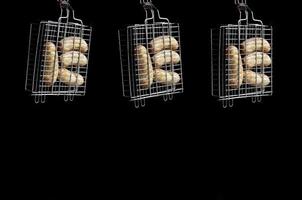A small hand grill is filled with fried thick sausages on a dark background photo