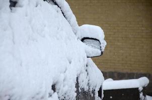 Fragment of the car under a layer of snow after a heavy snowfall. The body of the car is covered with white snow photo