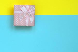 Small pink gift box lie on texture background of fashion pastel blue and yellow colors paper in minimal concept photo